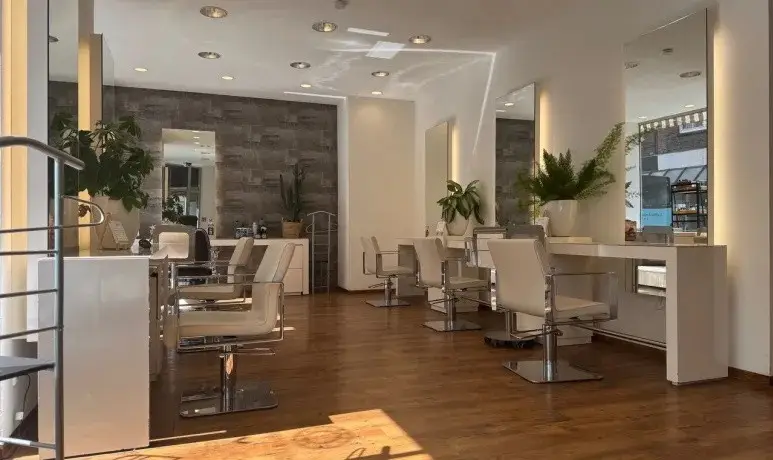 Blick in den hellen Salon der Haarschneiderei mit Holzboden, Spiegeln und Pflanzen